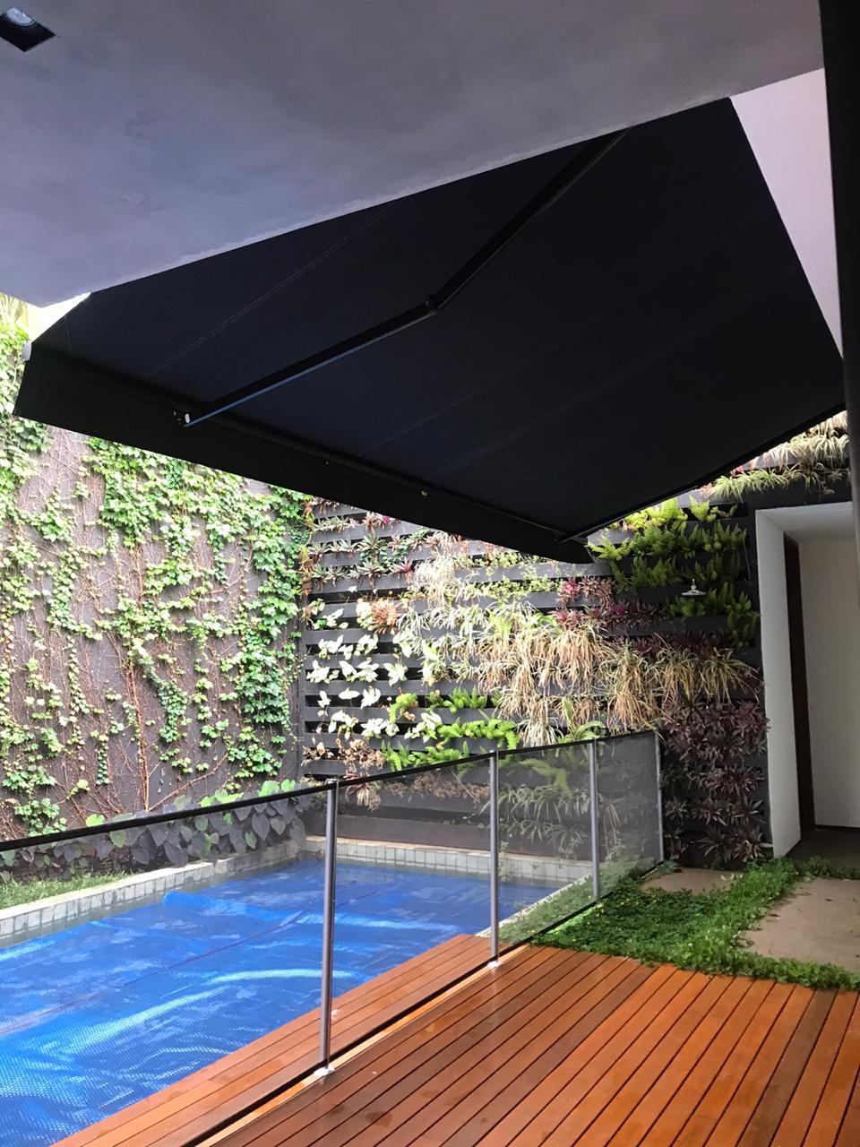 Toldo articulado sobre piscina com jardim vertical em Araçatuba